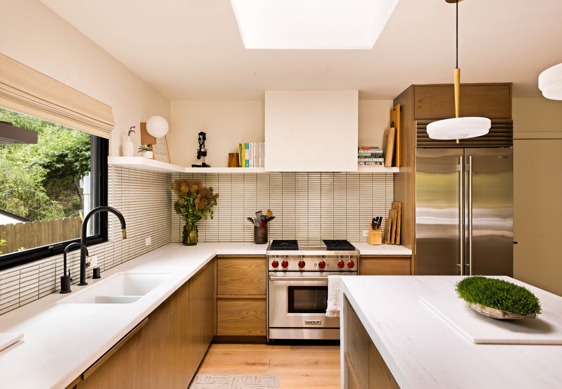Mandeville Canyon mid-century ranch house kitchen remodel.  Backsplash is white stacked ceramic tile with custom walnut wood cabinetry, painted white shelves with stacked books and plaster hood.