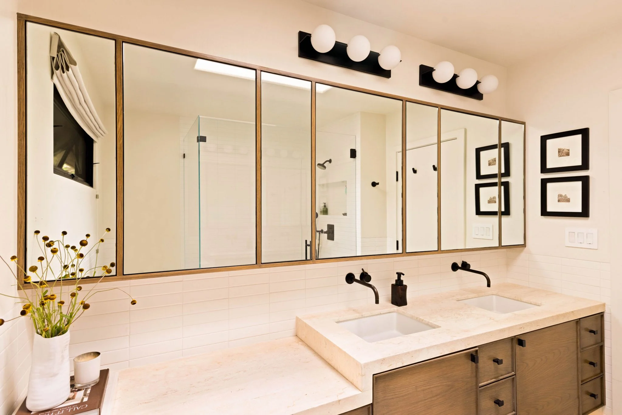 A bright, modern bathroom in a mid century modern home remodel.  A walnut floating vanity with a marble countertop.  The backsplash is horizontally stacked rectangular ceramic tiles.  There is a custom wall-to-wall walnut medicine cabinet above.