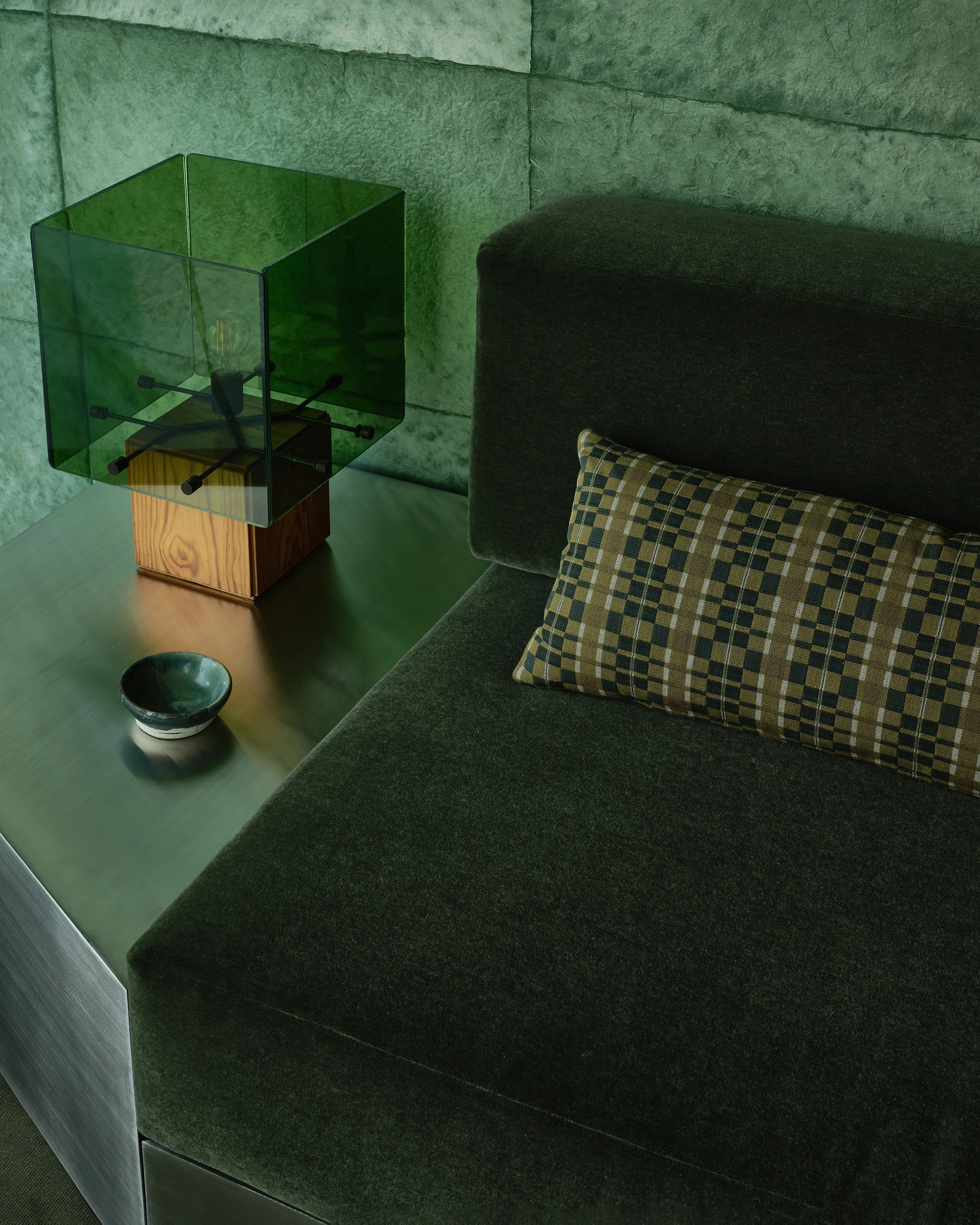 Comedian Anthony Jeselnik's home by Riccio Vidaurre Design.  A monochromatic teal green room with cannon bullock wallpaper, a stainless steel and mohair sofa and a vintage green glass lamp.