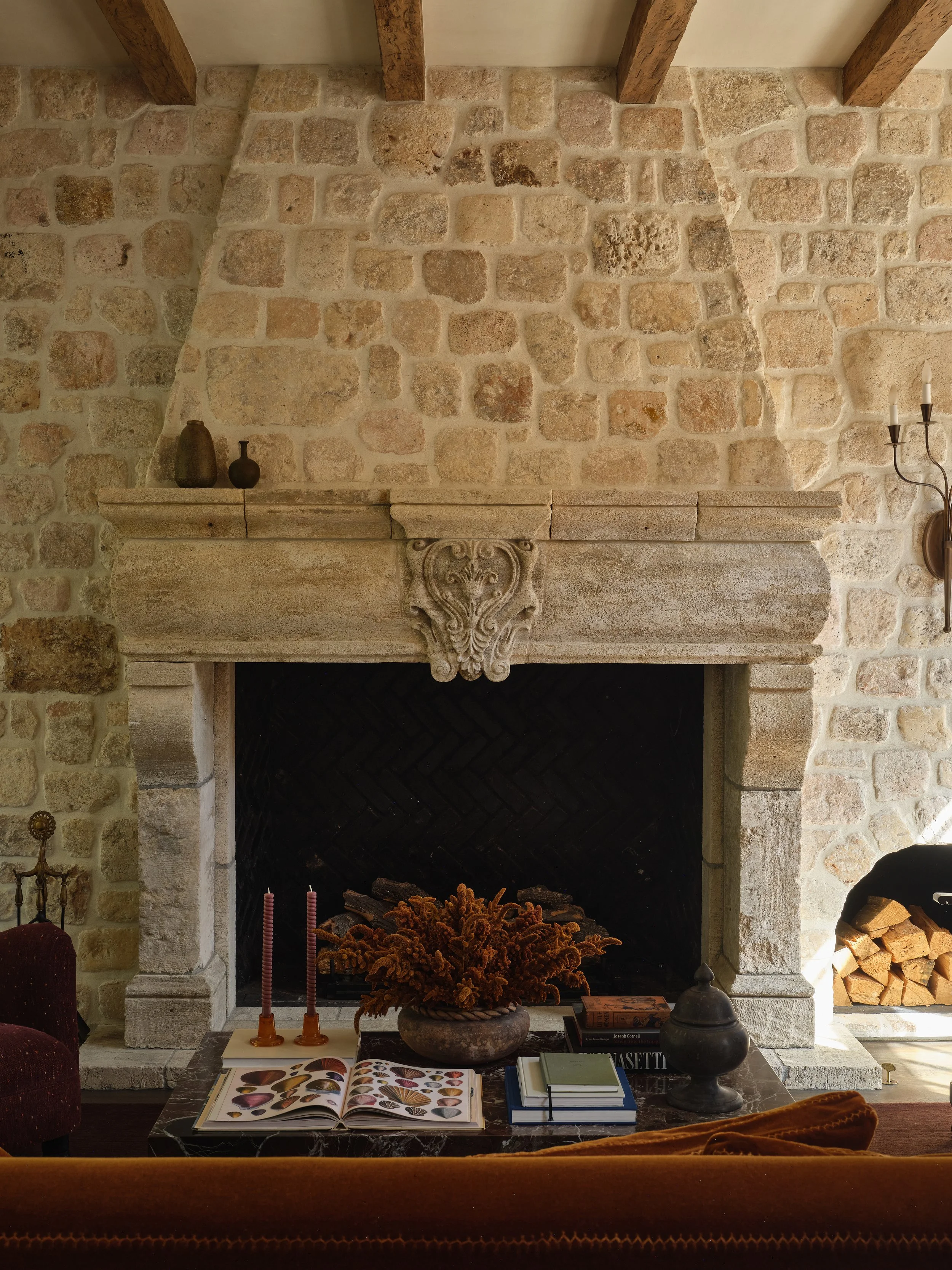 Living room with large stone fireplace, books, candles, and decorative items on coffee table.