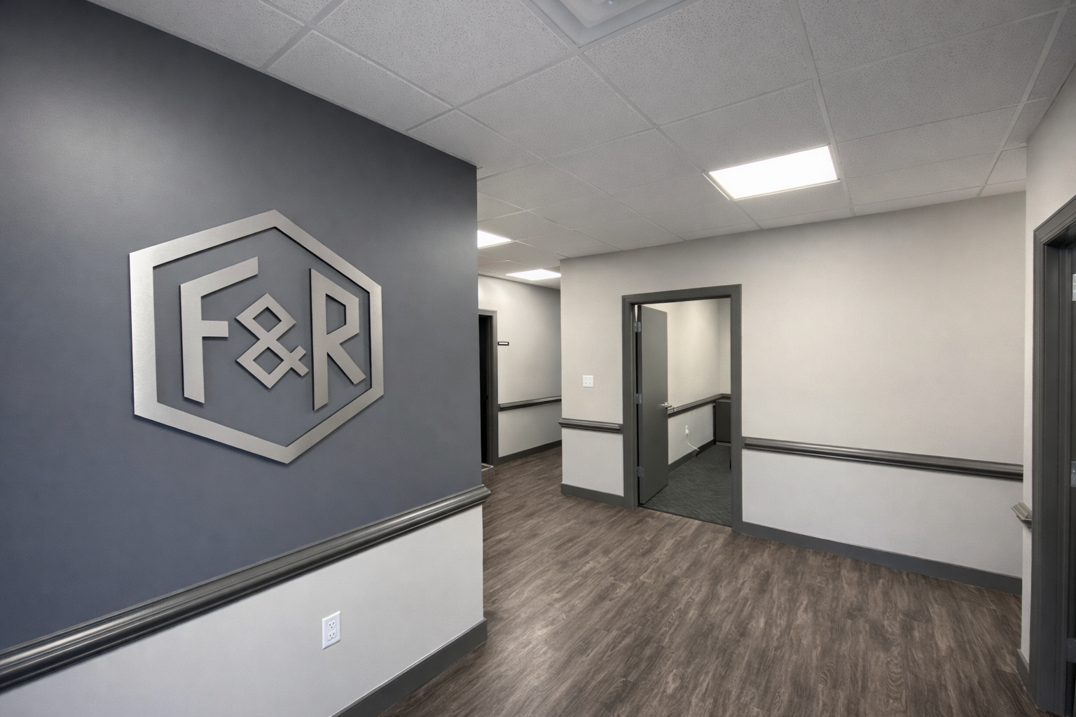 Office hallway with a blue accent wall featuring a large silver F&R logo, gray trim, and lighting fixtures on the ceiling.