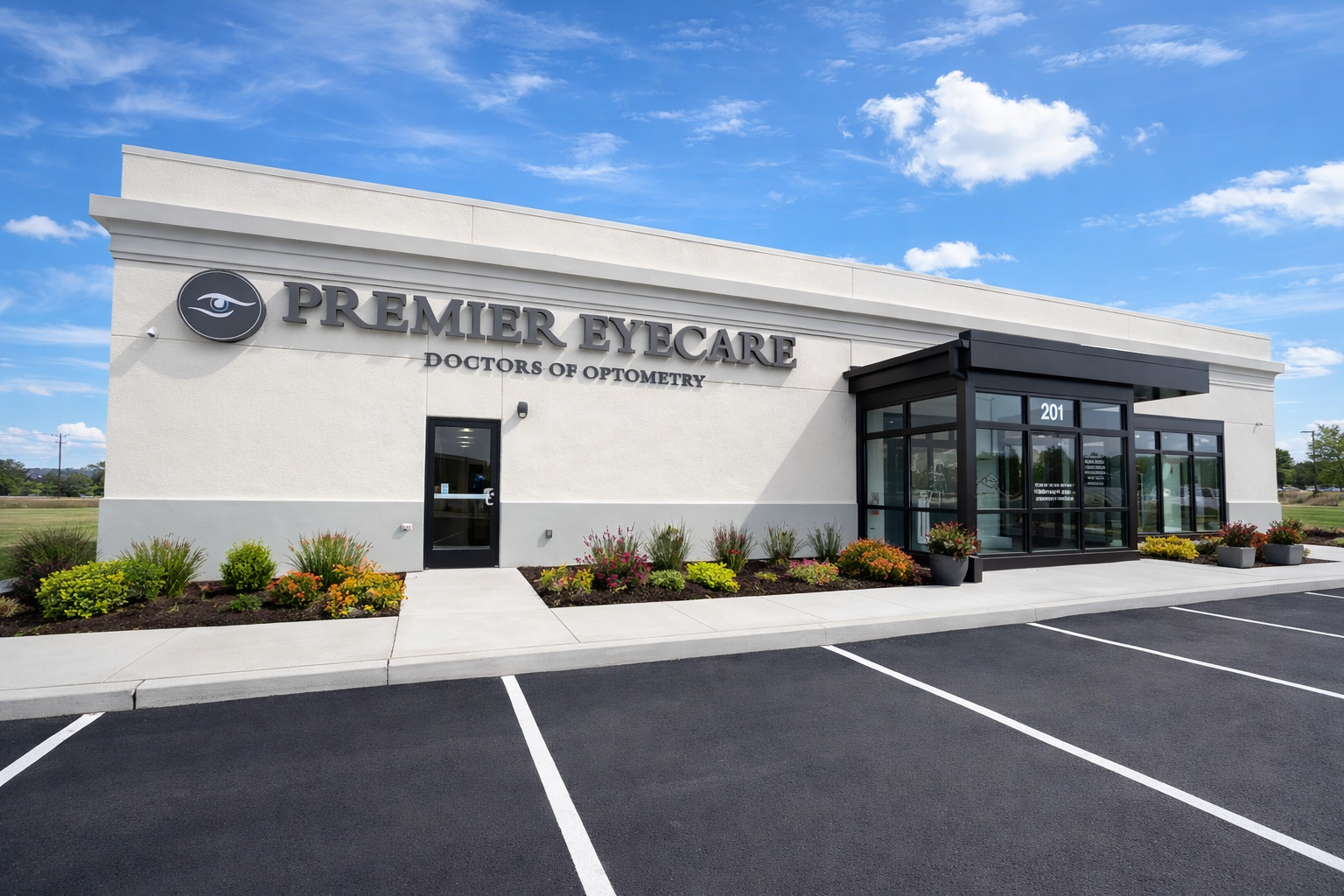 Exterior of a modern eye care clinic with the sign 'Premier Eyecare, Doctors of Optometry.' There are landscaped bushes and flowers, a glass entrance with the number 201, and a parking lot in front under a blue sky.