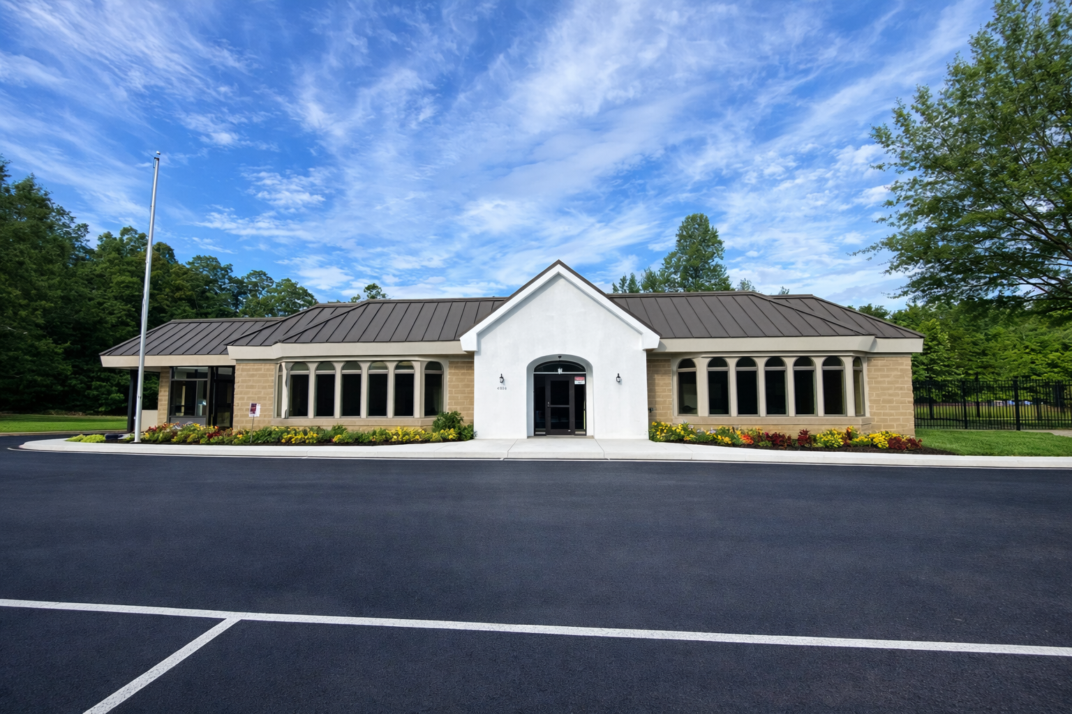 A single-story building with a white entrance, tan brick walls, and multiple arched windows surrounded by trees and parking lot.