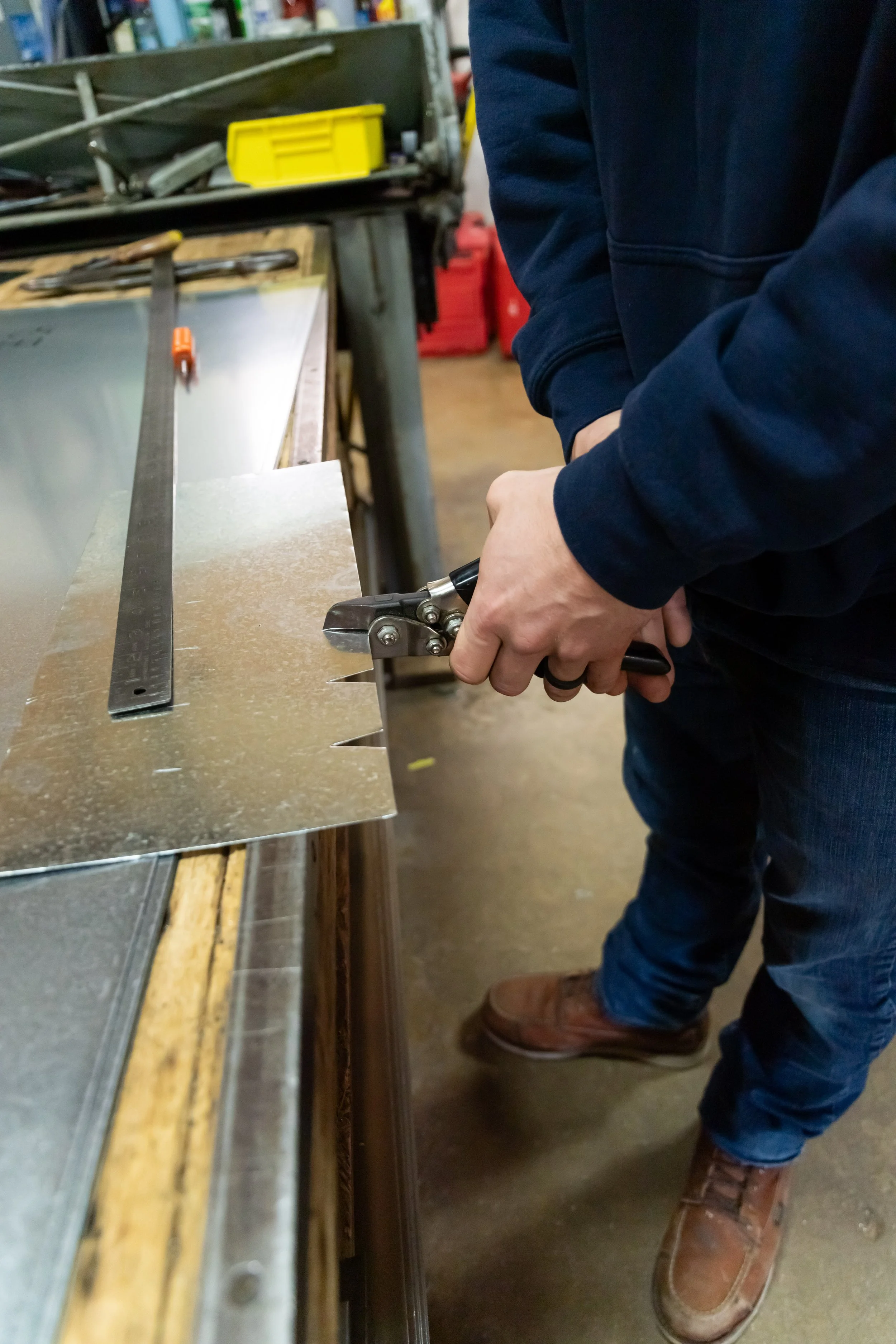 Devin Bilello working in a workshop  on sheet metal, with various tools and supplies on a workbench.