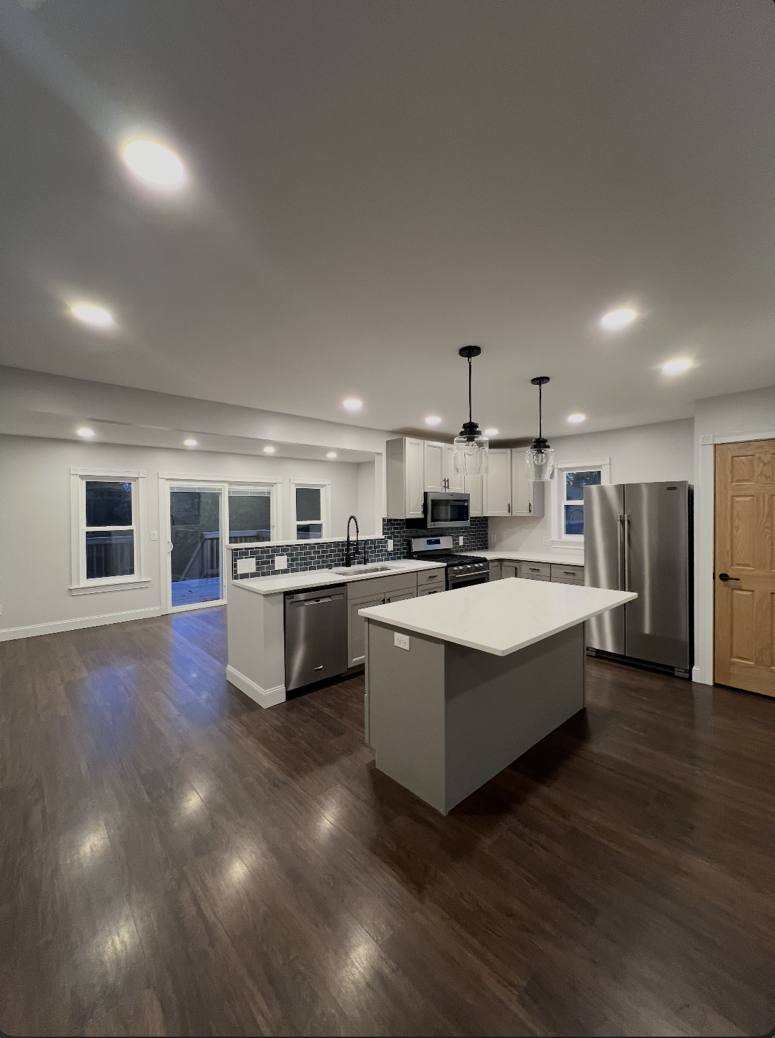 Modern kitchen with white cabinets, stainless steel appliances, a central island, dark hardwood flooring, and pendant lighting. DRB Services, home remodel hvac systems.