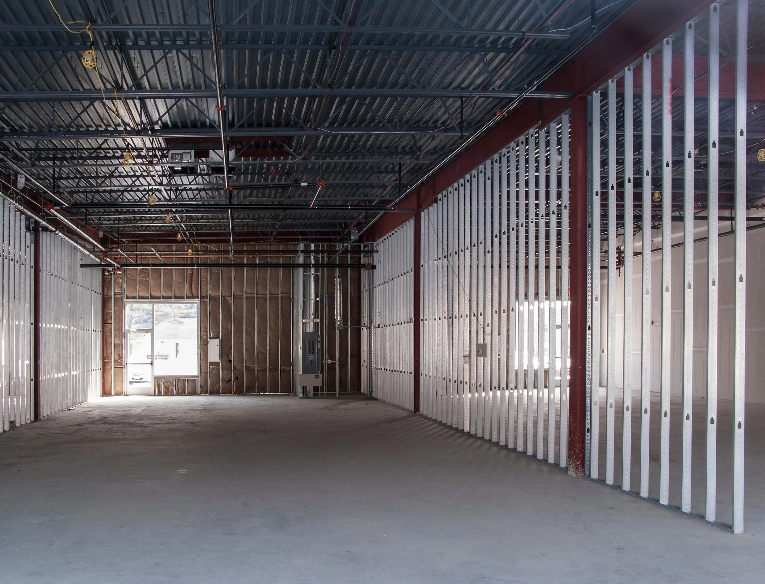 Interior view of a building under construction with metal framing, electrical wiring, and exposed ceiling trusses.