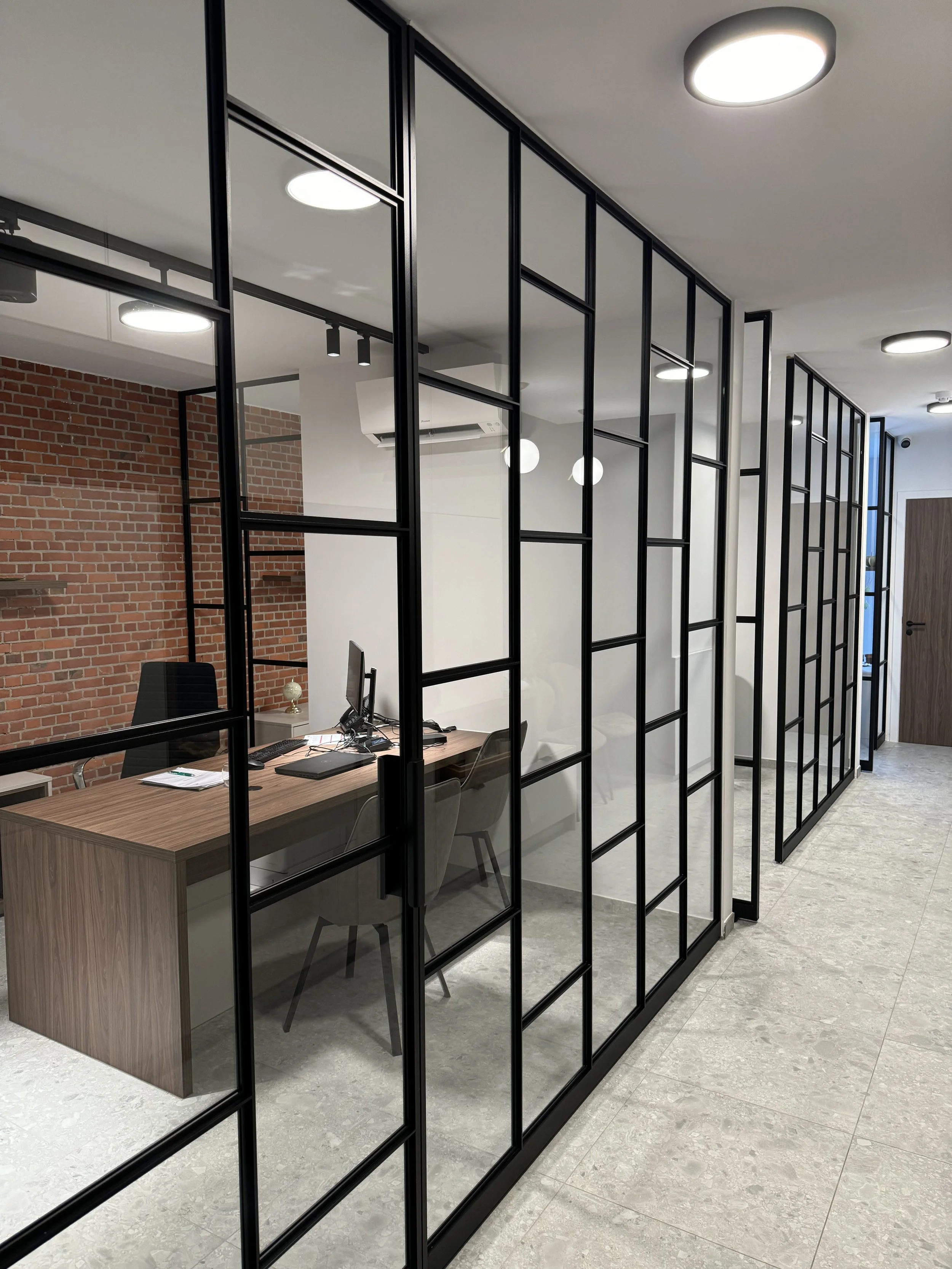 Een kantoorruimte afgezet met zwarte metalen scheidingswanden die proper gekuist is door ramenwassers.
