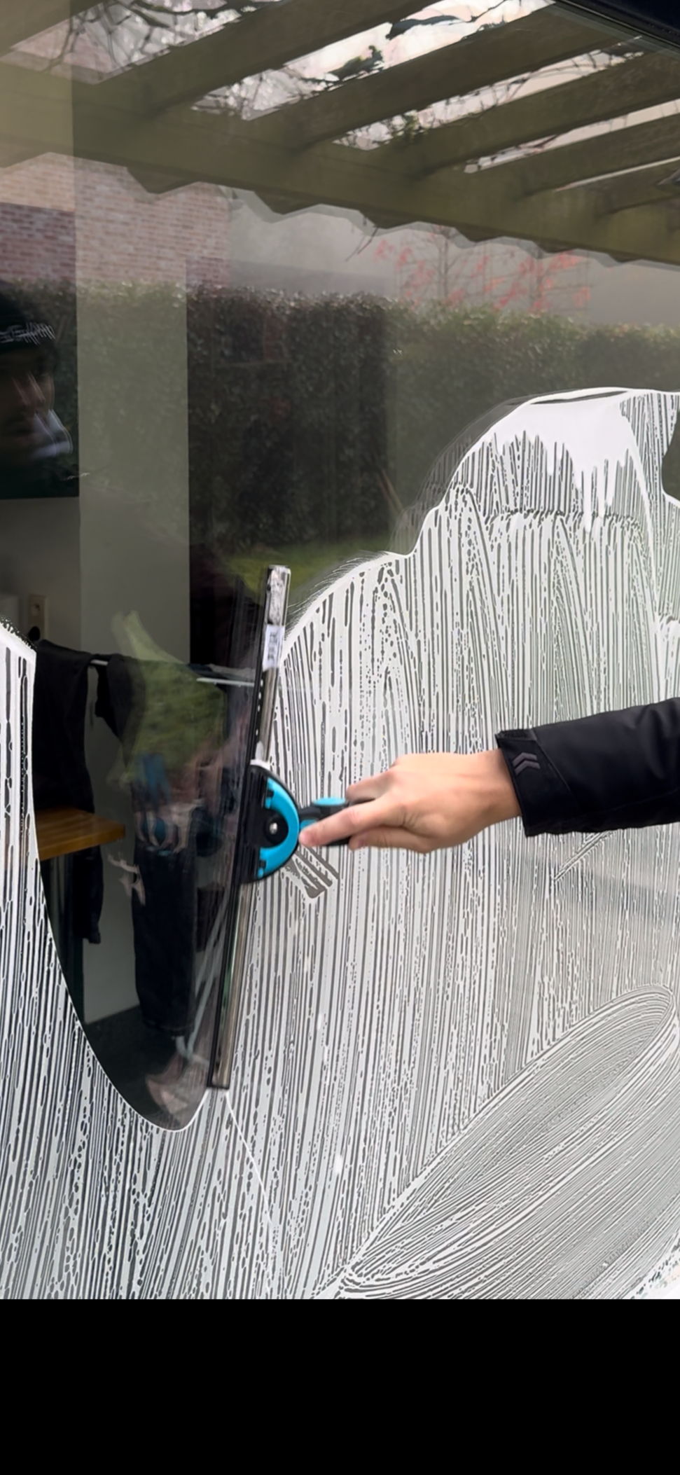 Een persoon die een glas schoonmaakt met behulp van een aftrekker en zeep.