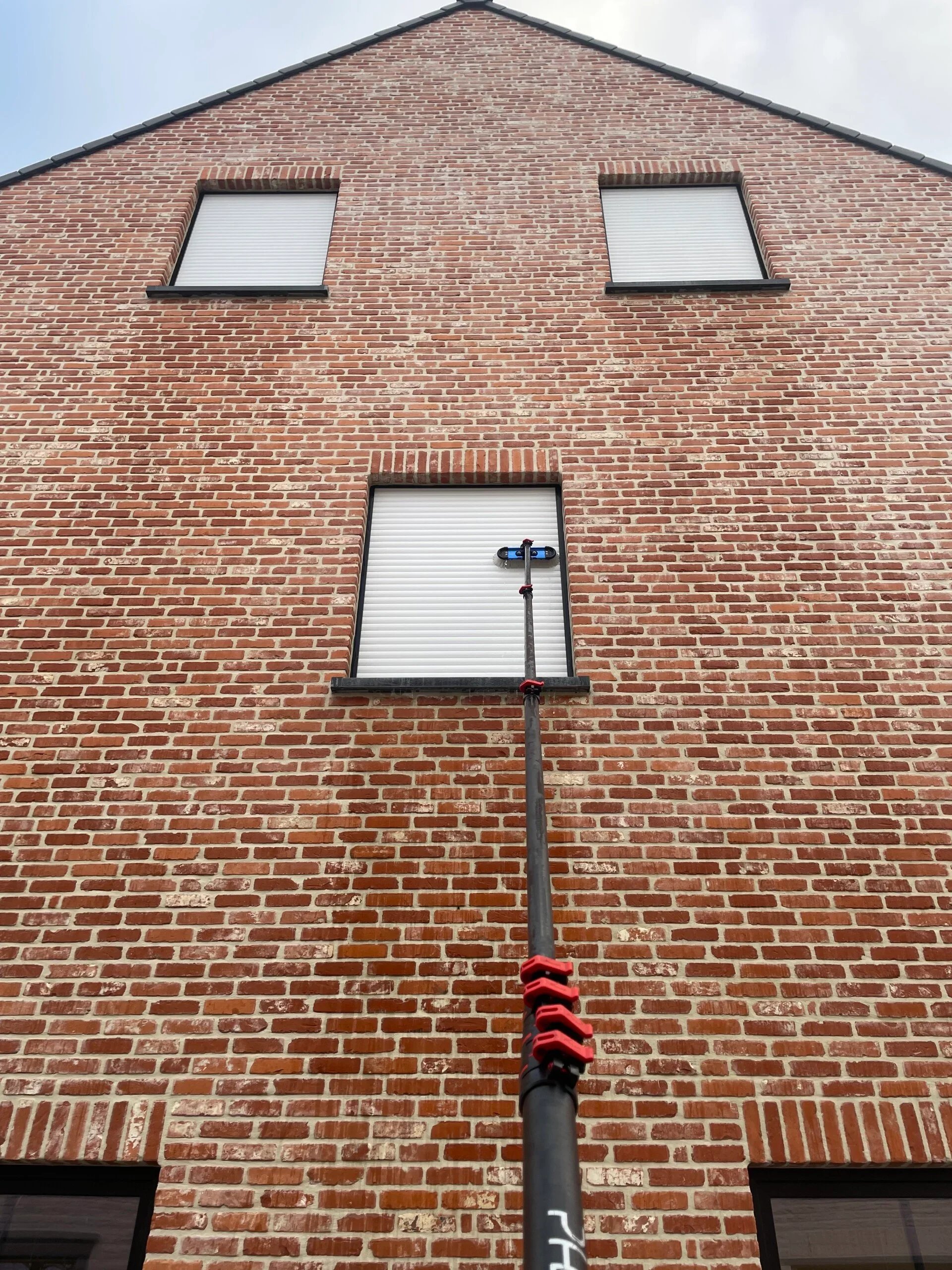 Drie hoge ramen met gesloten rolluiken die gereinigd worden. 