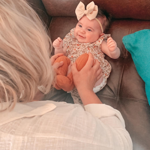 A chiropractor checking a baby's hip mobility, with a smiling baby girl lying on a brown couch.