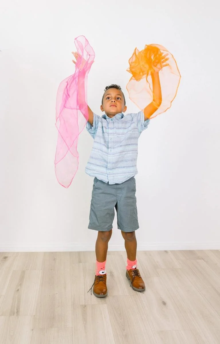 Young boy raising colorful sensory scarves overhead during a movement activity.