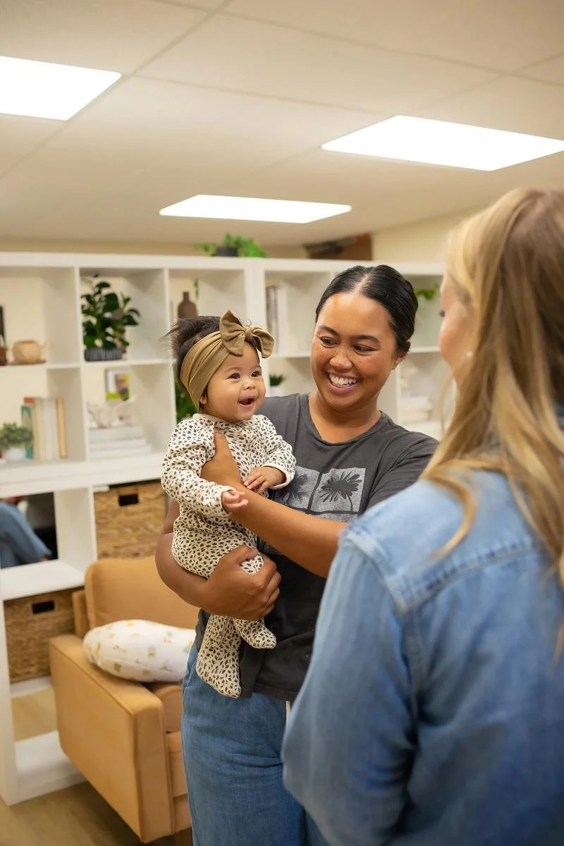 A parent holding a baby who reaches toward another family member in the office