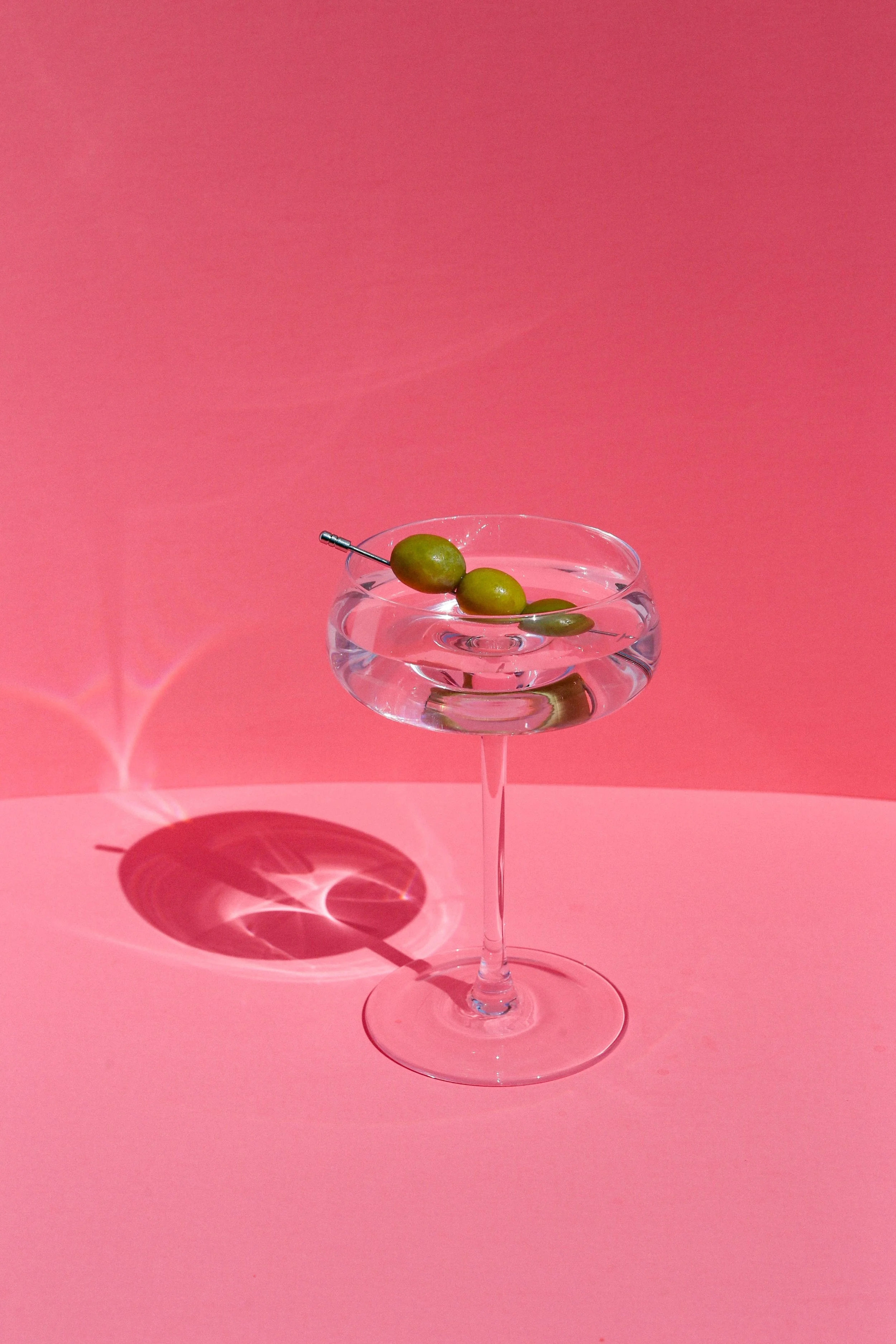 A cocktail glass with water and OS in a pink setting, casting a circular shadow.