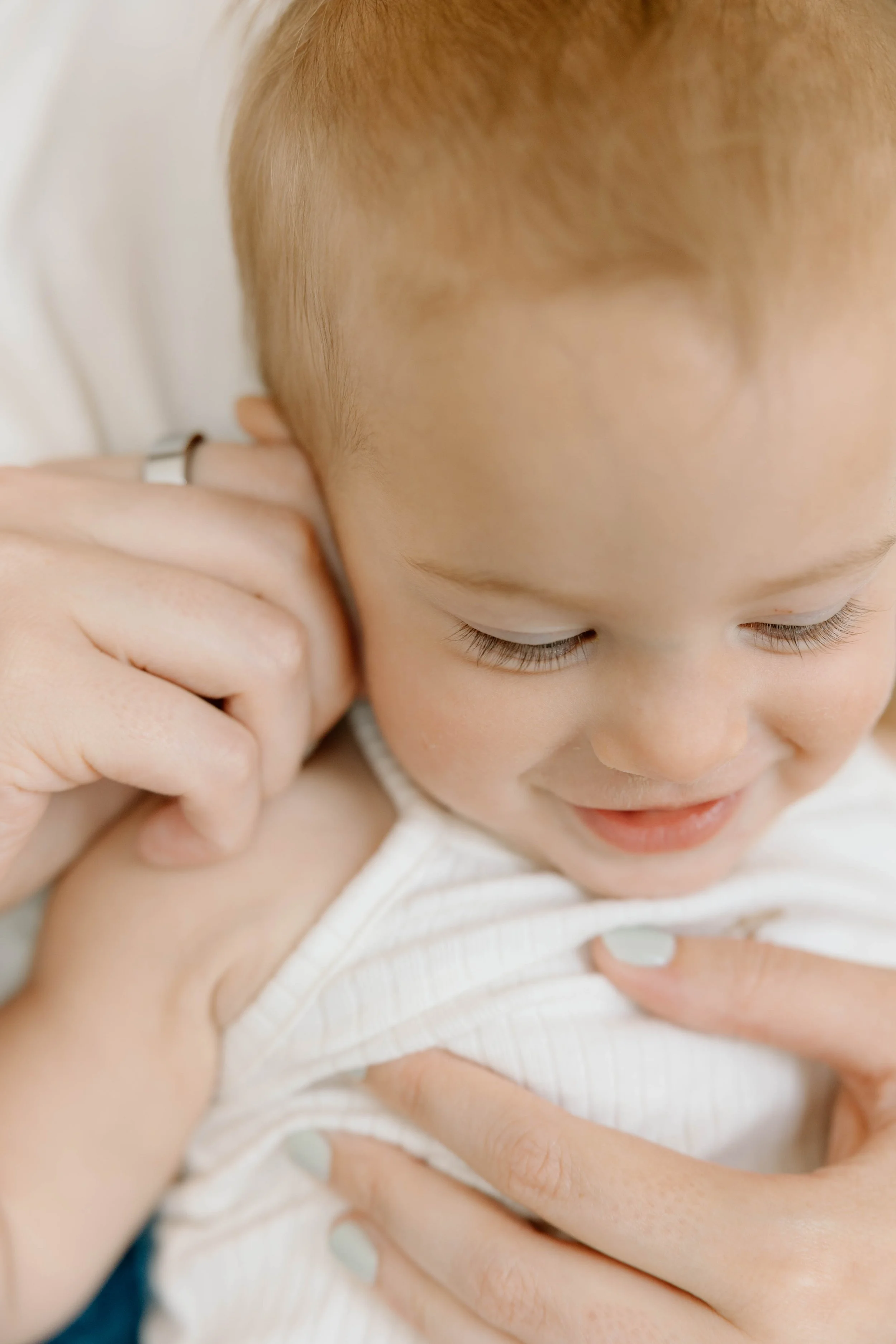 A close-up of a young child being held and adjusted by a chiropractor in Temecula, CA. Focus is on the child's face with closed eyes and a gentle smile, wearing a white sleeveless top.