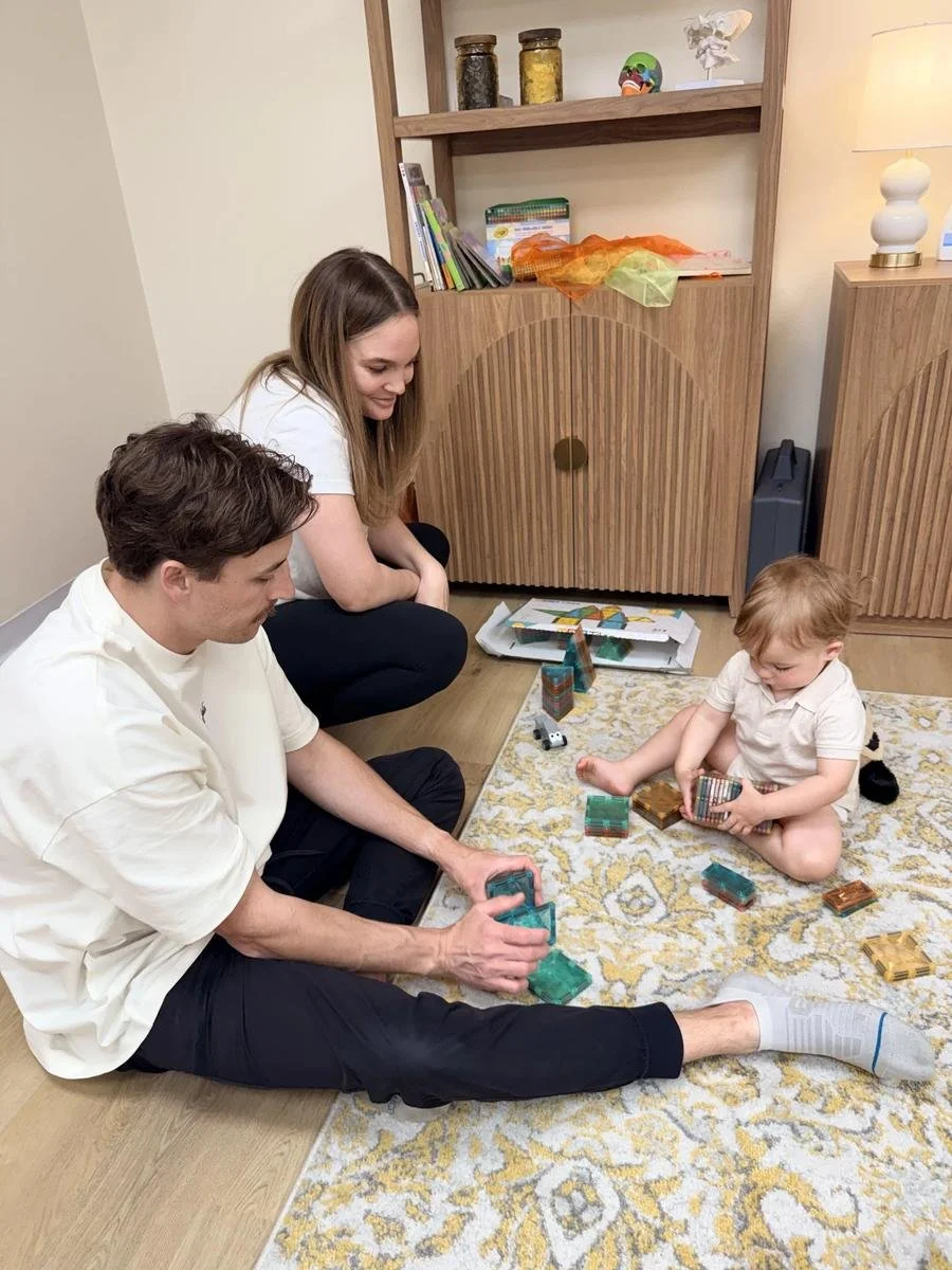 Two adults playing with a toddler in the Taproot Chiropractic kids’ area.