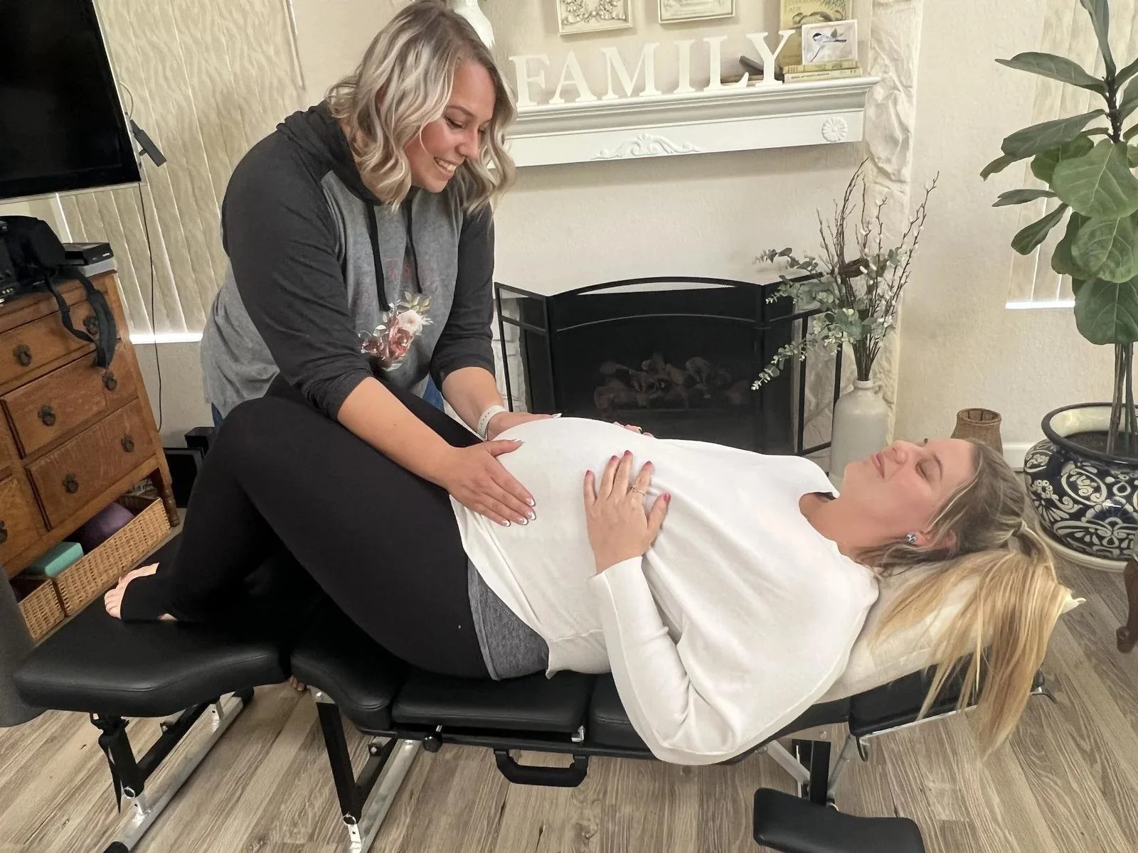 Dr. Jennifer Gordon providing a prenatal adjustment to a pregnant patient reclining on a chiropractic table near a fireplace.