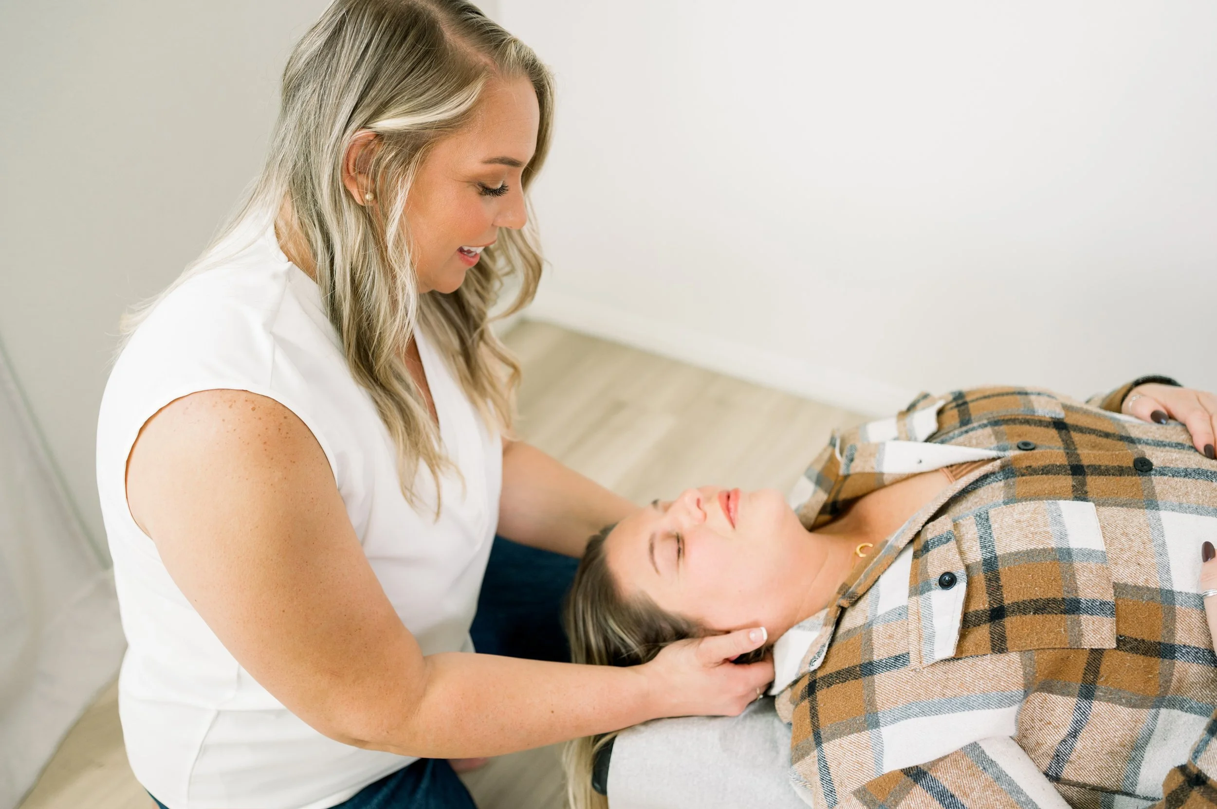 A woman providing chiropractic care to another woman lying on a treatment table, with her eyes closed.