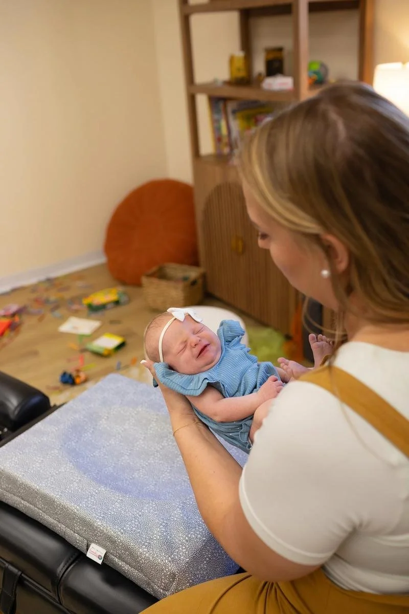 A chiropractor holding an infant above a padded treatment table.
