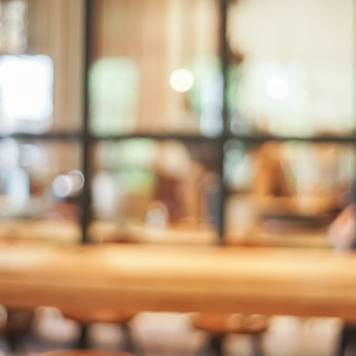 Blurred view of a cozy indoor space with wooden furniture and large windows letting in natural light.