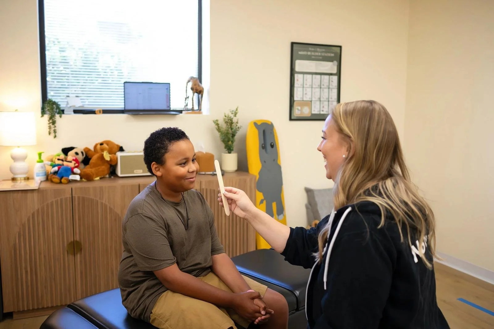 Dr. Jennifer Gordon holding a visual target in front of a seated child during a pediatric assessment at Taproot Chiropractic.