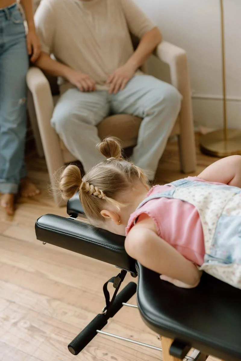 Young girl lying face-down on a chiropractic treatment table with adults seated nearby.