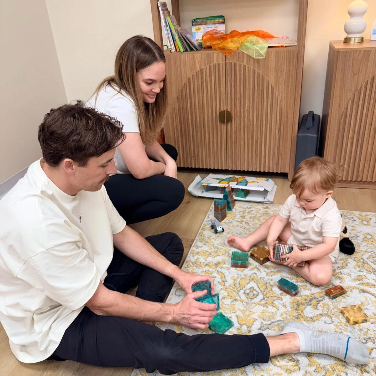 Two adults playing with a toddler and magnetic building tiles in the Taproot Chiropractic kids’ area.