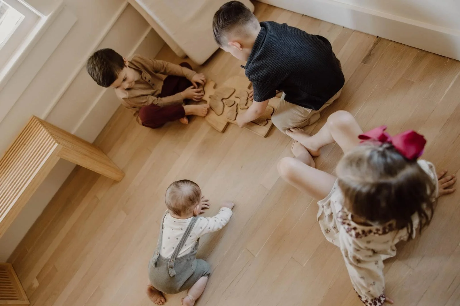 Four children playing together with wooden puzzles on the floor.