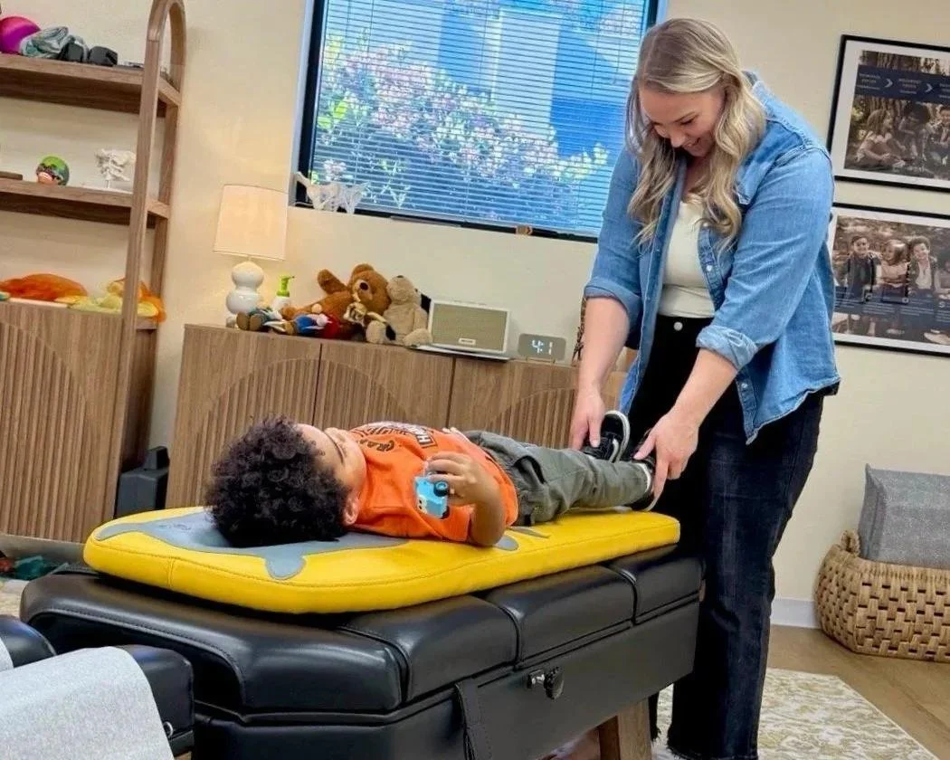 Dr. Jennifer Gordon checking a young child’s leg alignment while the child lies on a pediatric chiropractic table.