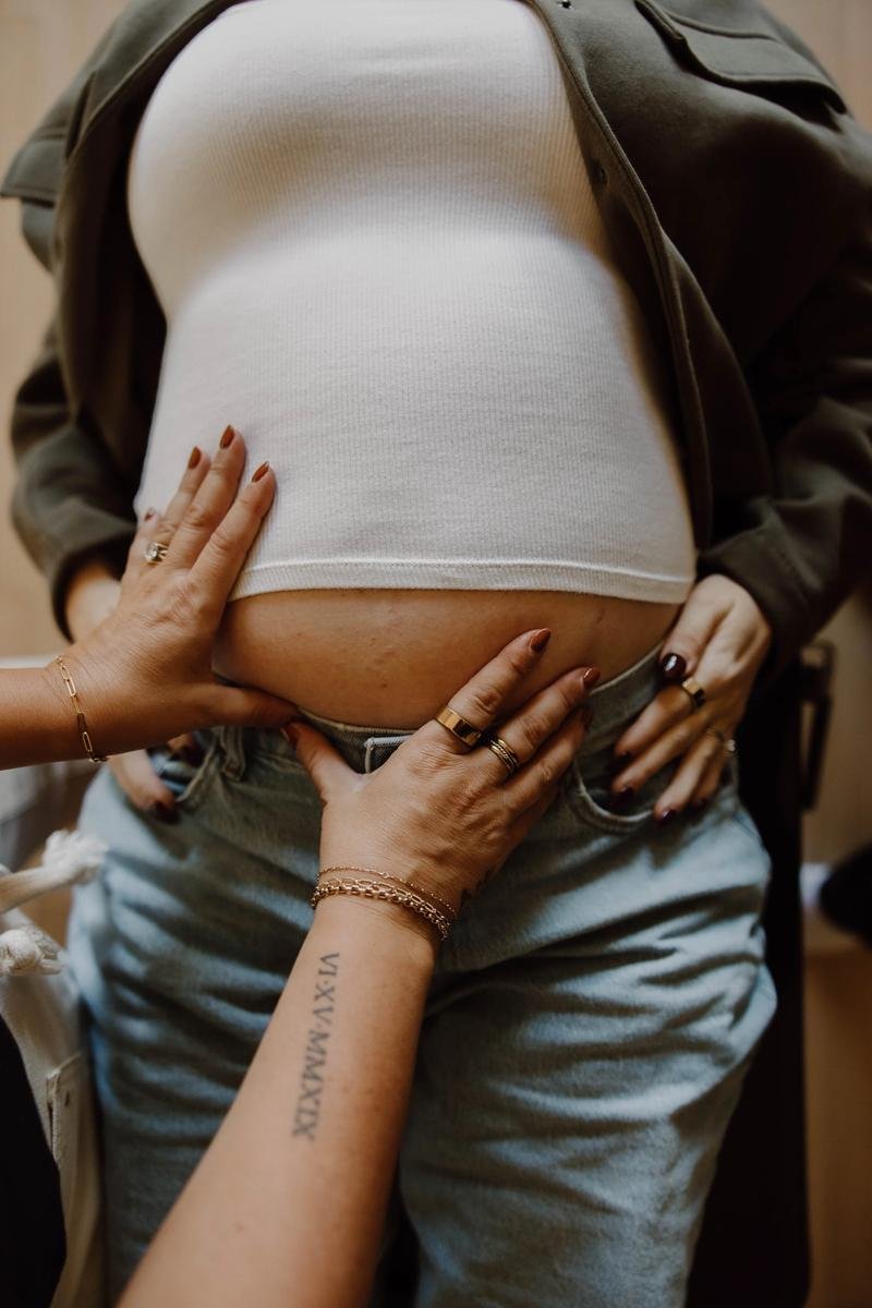 : Close-up of hands placed gently on a pregnant patient’s lower abdomen.