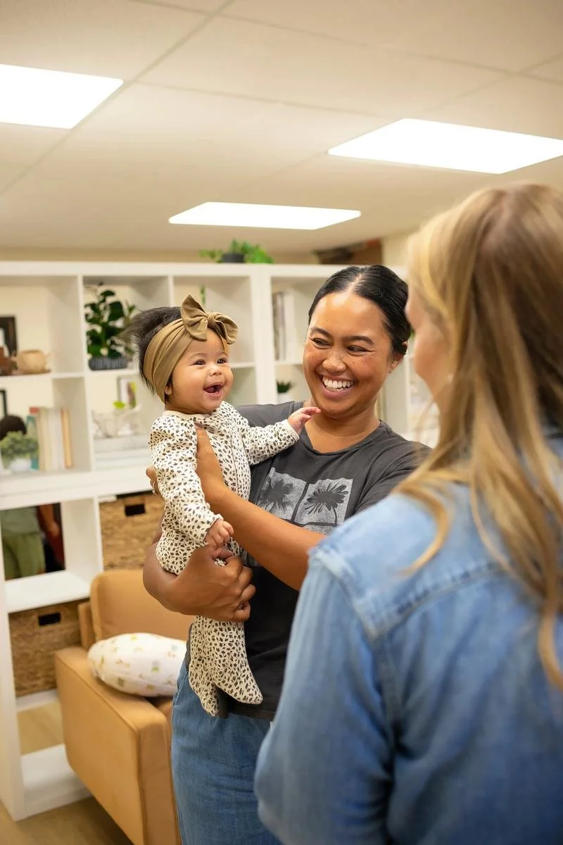 Dr. Jennifer Gordon talking with a mother holding her baby in the Taproot Chiropractic office.