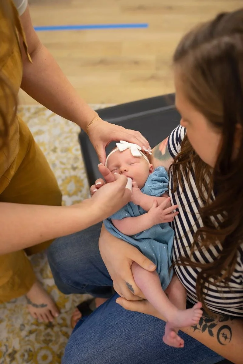 Dr. Jennifer Gordon performing a gentle oral assessment on an infant while the baby is held by a parent at Taproot Chiropractic.