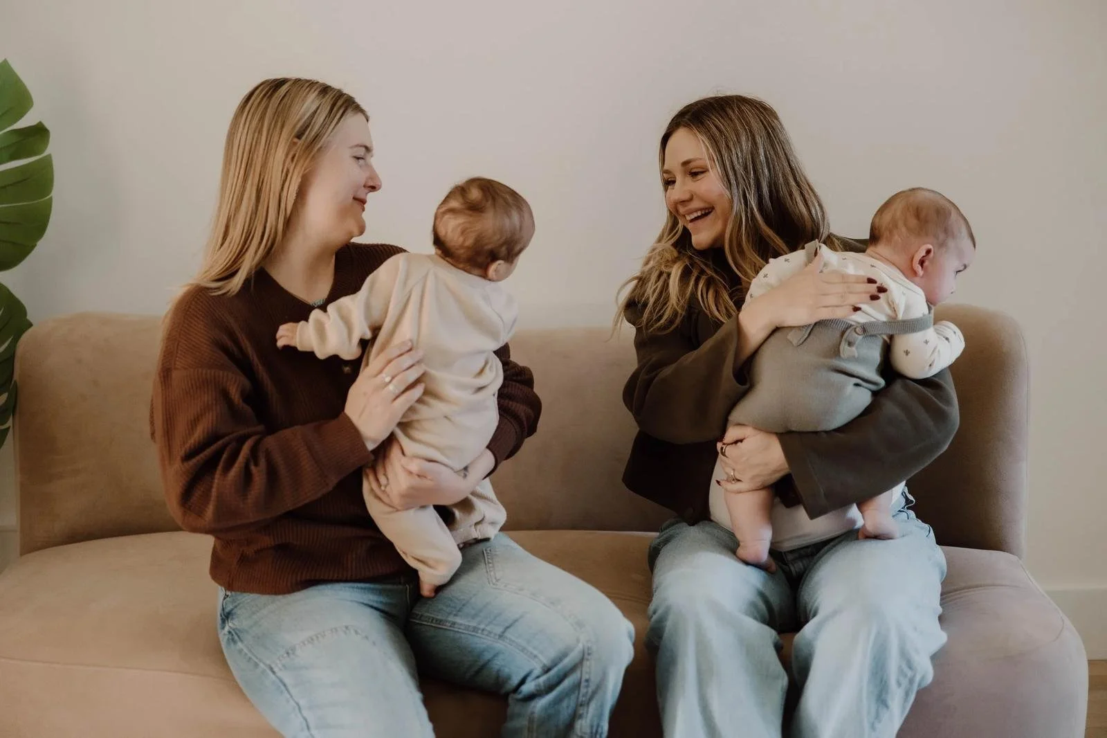 Two mothers sitting together on a couch while each holds a baby.