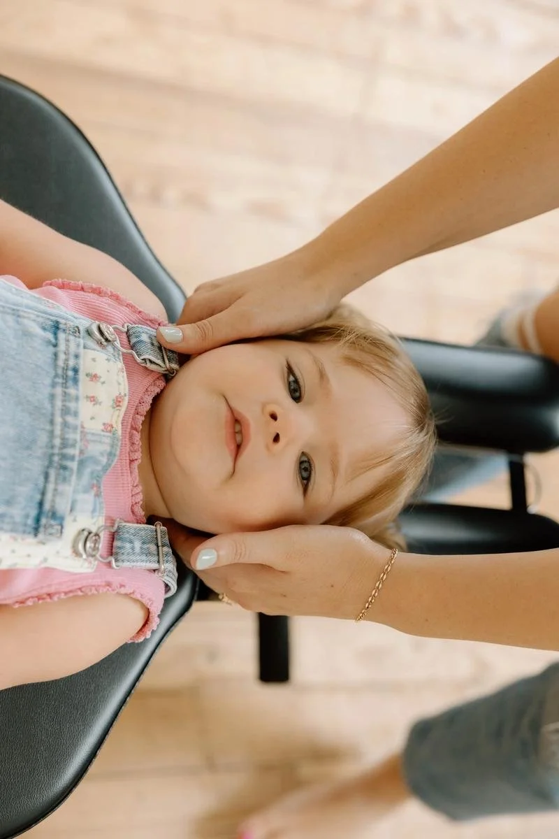 Chiropractor gently supporting a young child’s head and neck while the child lies on a chiropractic table.