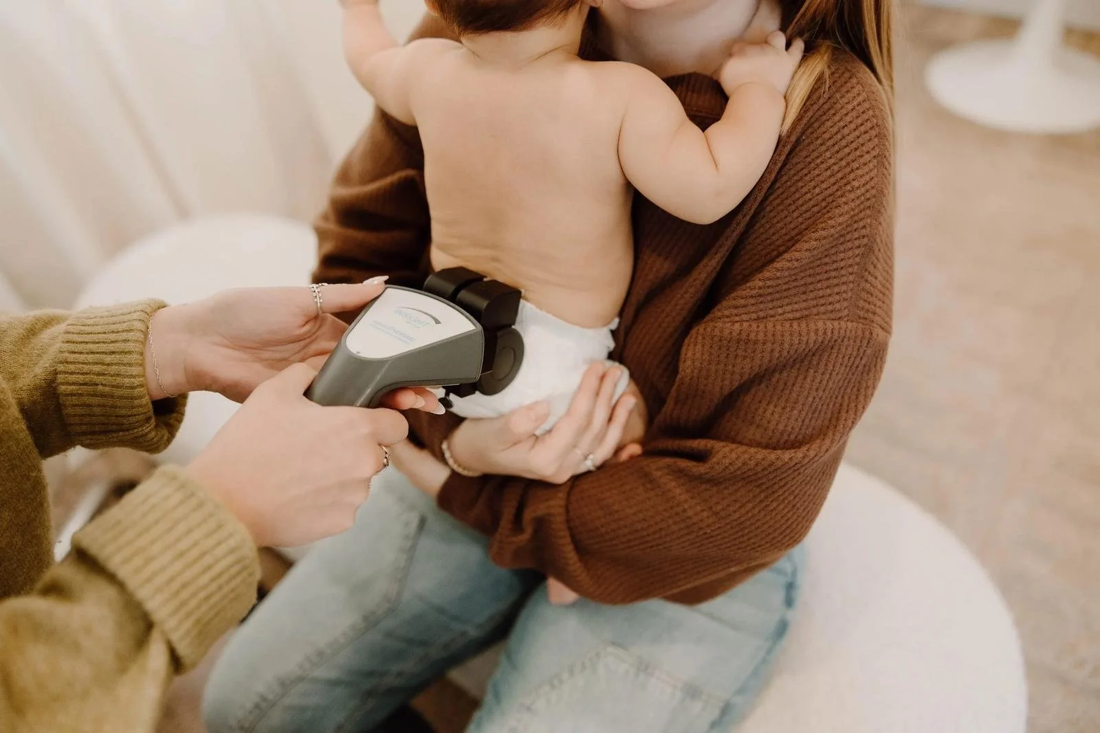 Dr. Jennifer Gordon using a handheld scanning device on an infant's spine held by a parent