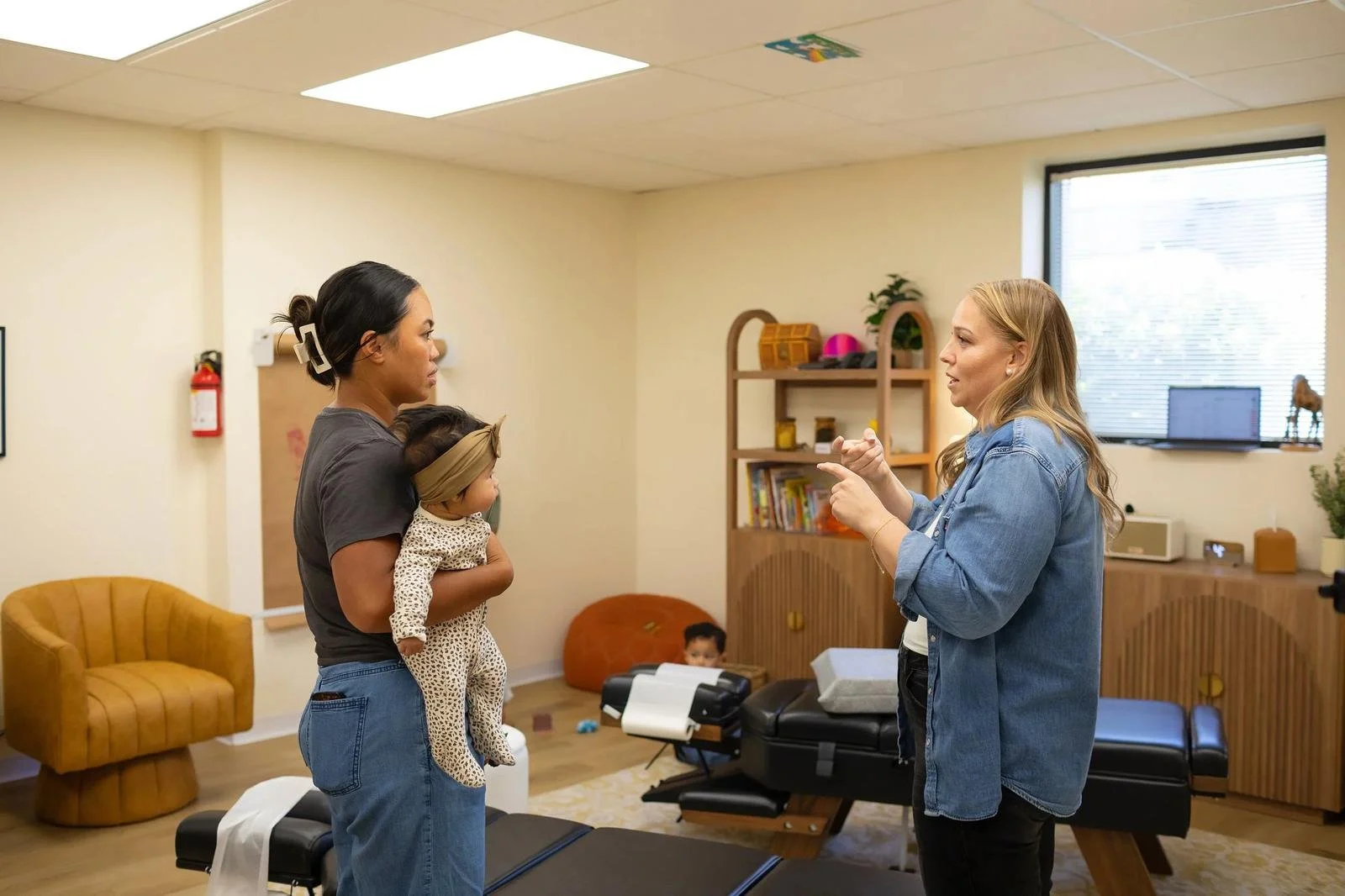 Two practitioners consulting near a treatment table while a parent holds a baby in the office