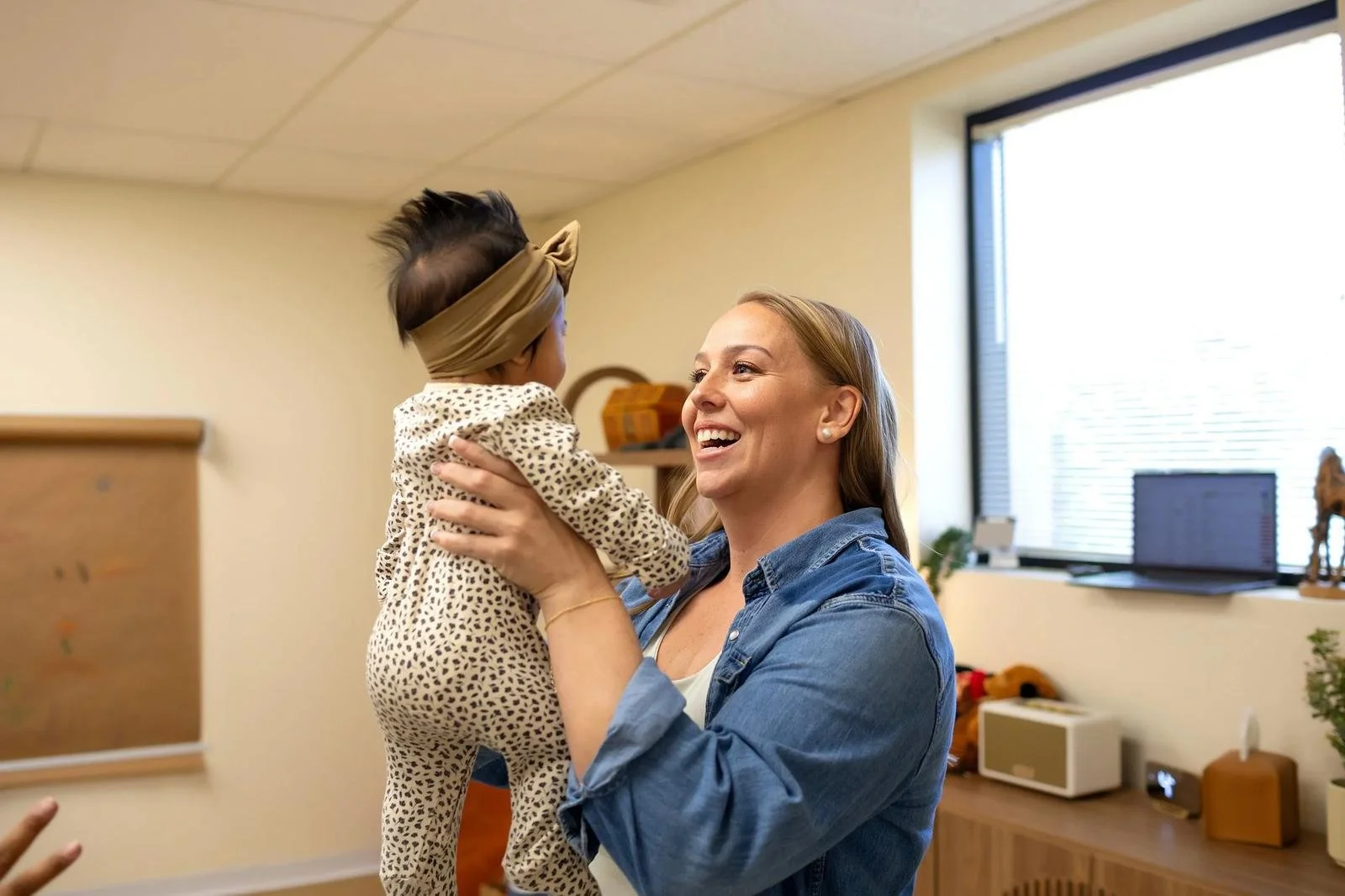 Dr. Jennifer Gordon smiling while holding an infant upright in the pediatric treatment room at Taproot Chiropractic.