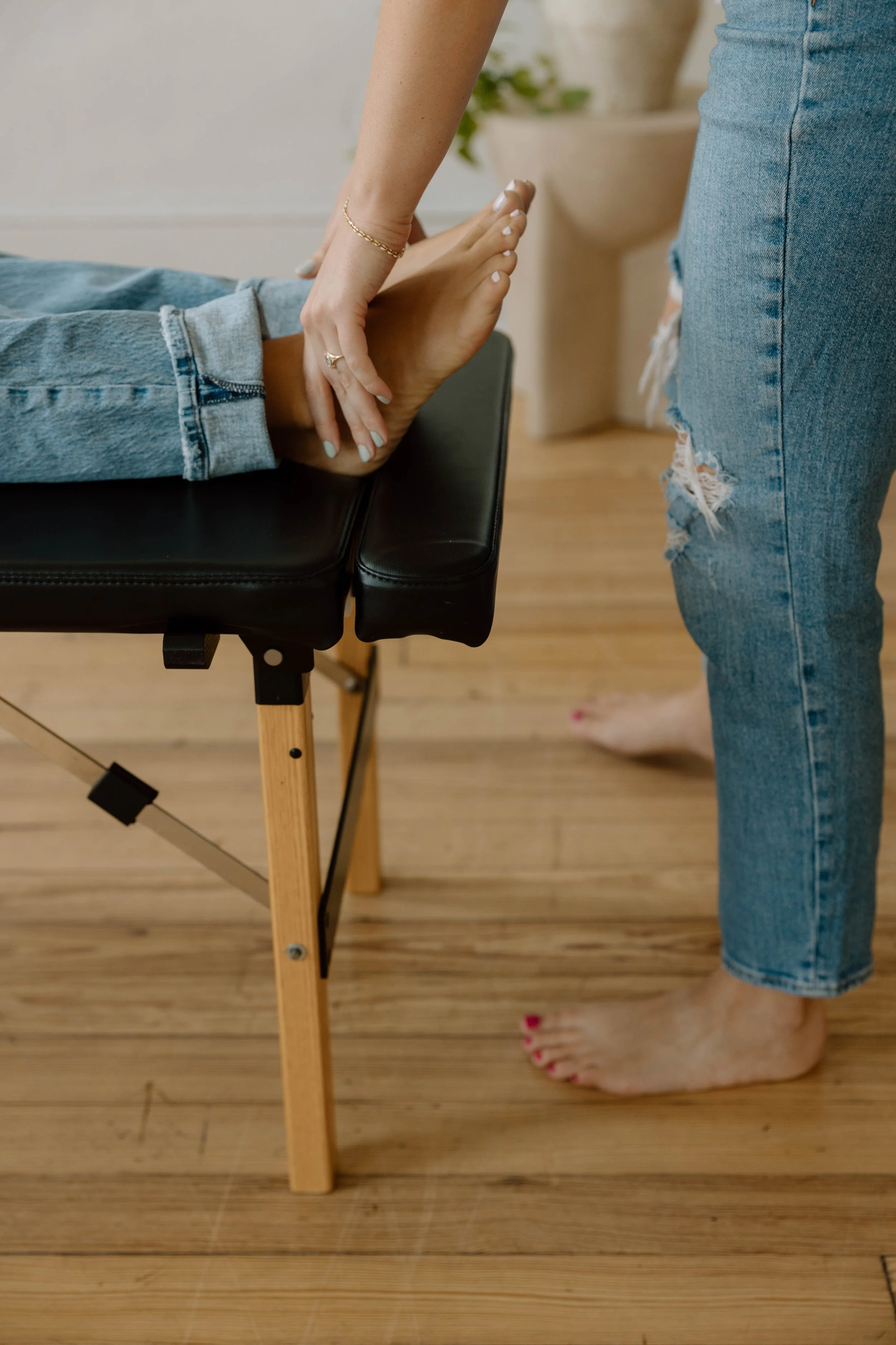 A person in jeans receiving a leg check by a chiropractor while laying face up on a chiropractic table.
