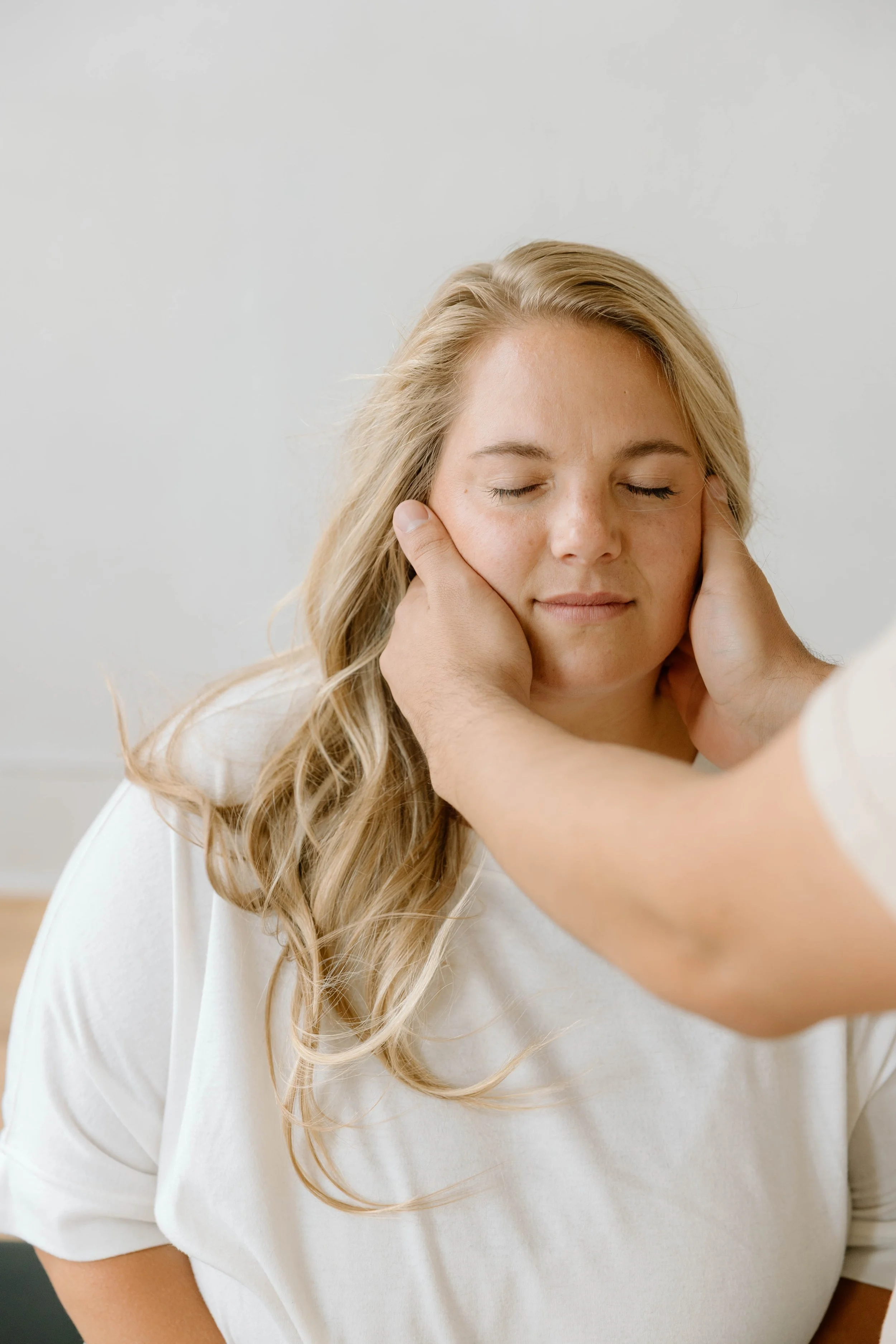 A woman with long blonde hair has her eyes closed as a chiropractor gently holds her neck, performing a relaxing chiropractic adjustment.