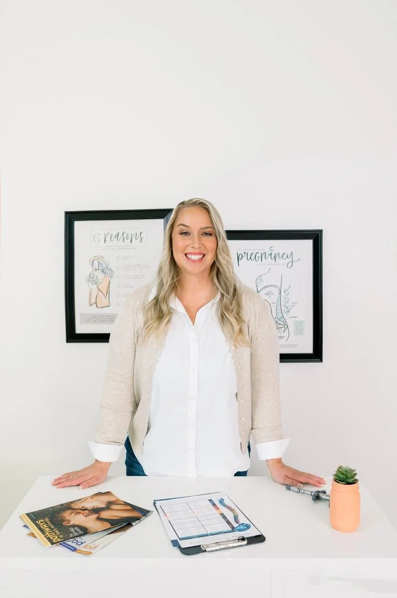 Dr. Jennifer Gordon standing at a table with printed materials, framed diagrams on the wall behind her