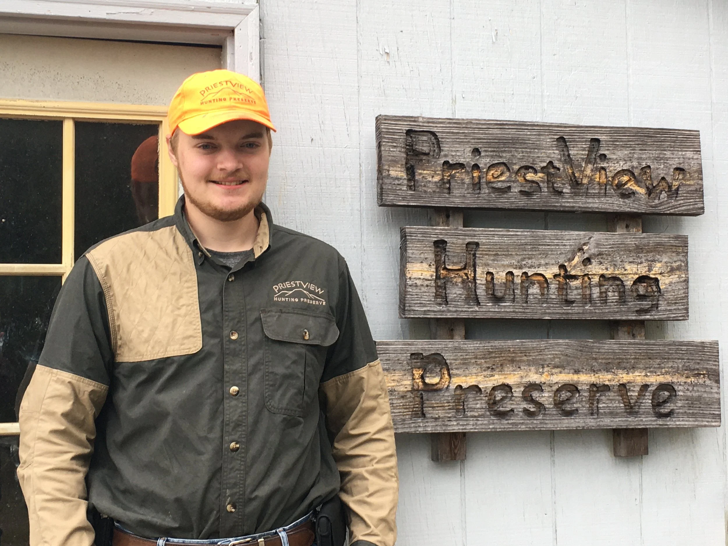 Photo of Field Manager Gabe Tomson in front of wooden PreistView Hunting Preserve sign.