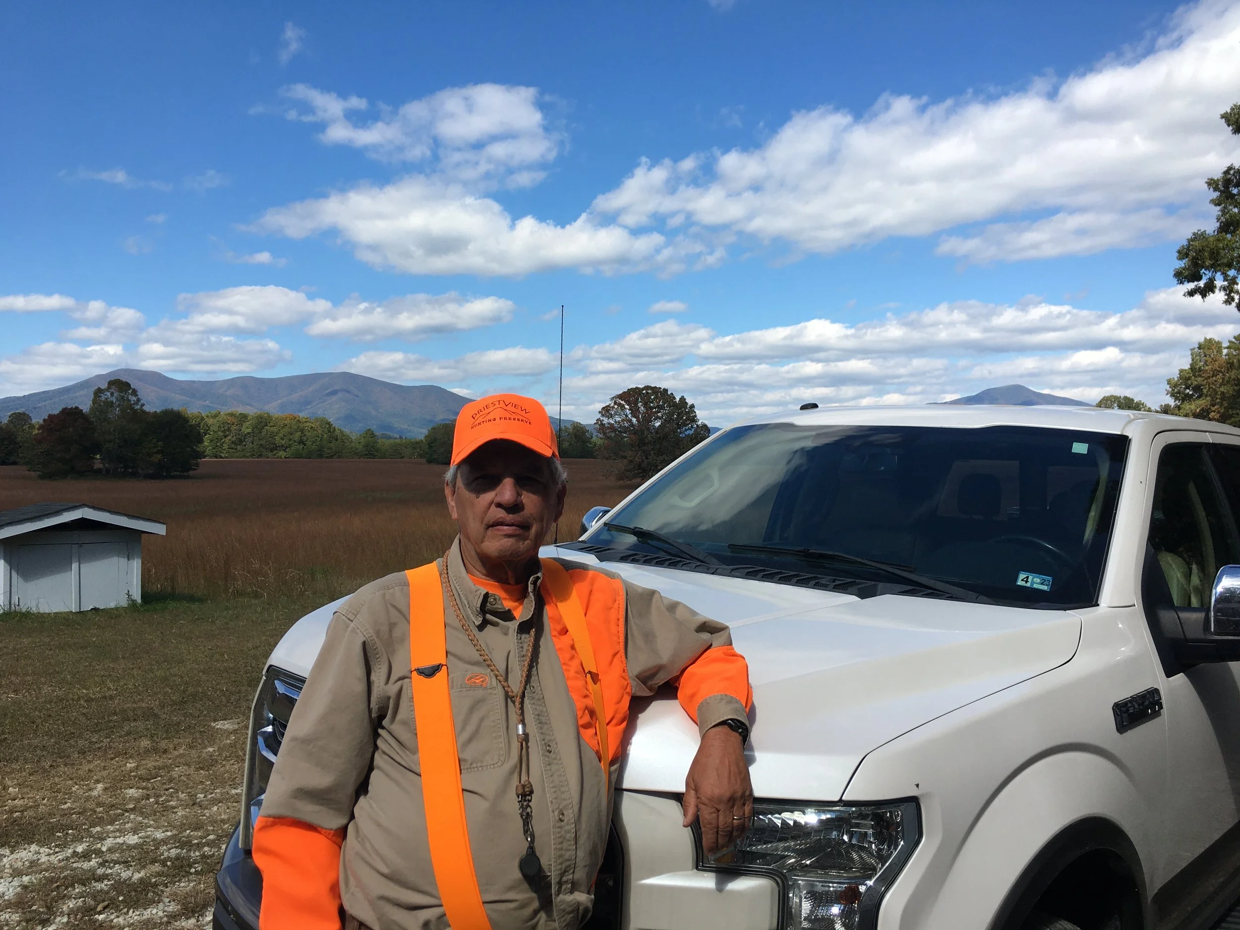 Photo of Bill Berkley in a blaze orange hunting shirt in front of a white pickup truck