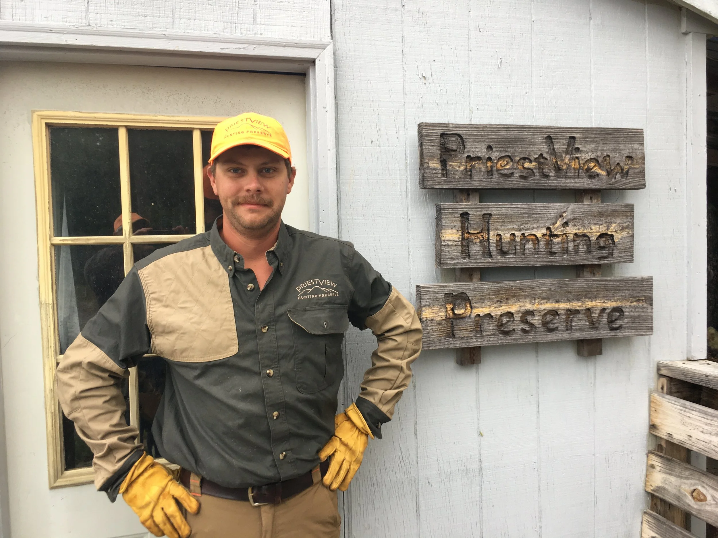 Photo of Cody Ott next to the wooden PriestView Hunting Preserve Sign
