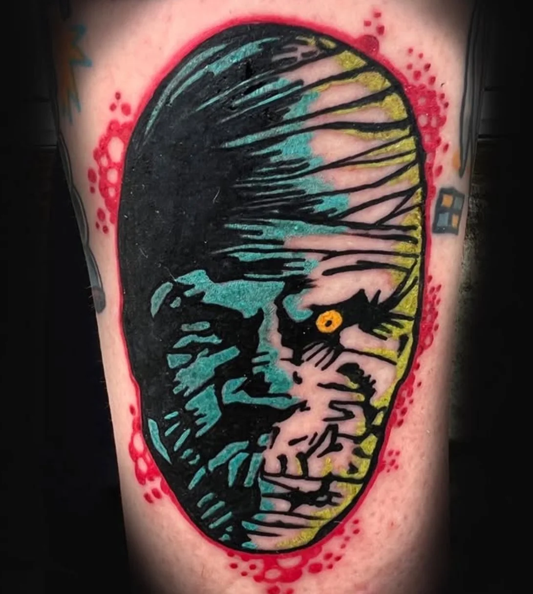 Tattoo of a stylized face resembling the mummy with vibrant colors and bold outlines.