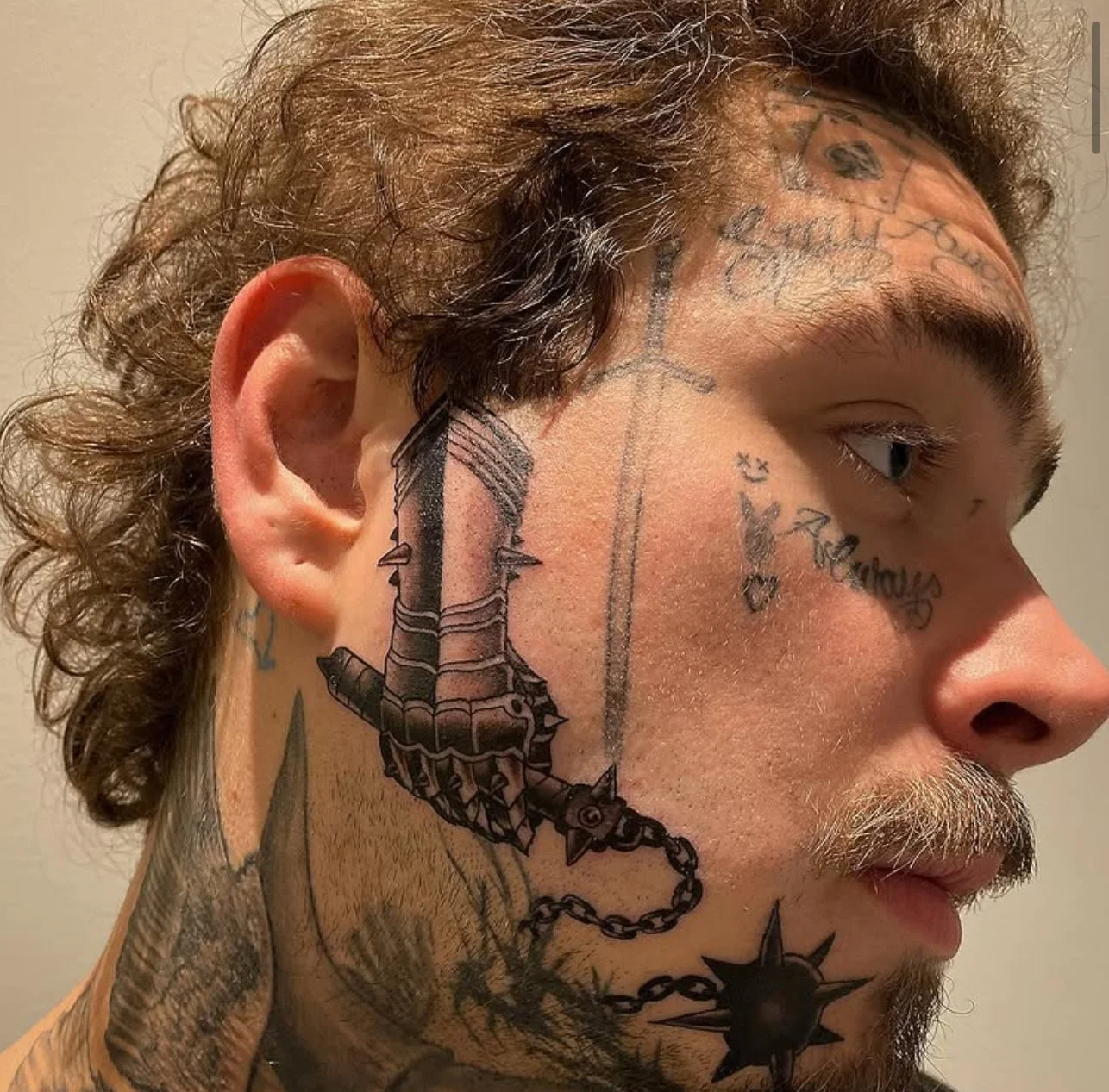 Close-up of Post Malone with multiple tattoos on his face, neck, and head, including a large tattoo of a chain with a mace on his neck and a dagger on his forehead.