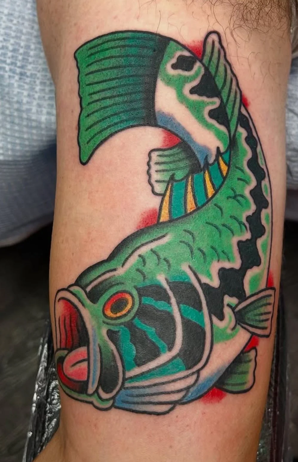 Colorful tattoo of a large mouth with green, black, white, and orange markings, detailed fins, and an open mouth.