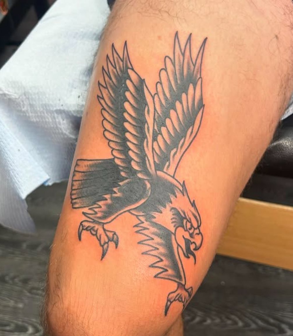 Black and gray tattoo of an angry eagle in flight on a person's arm.