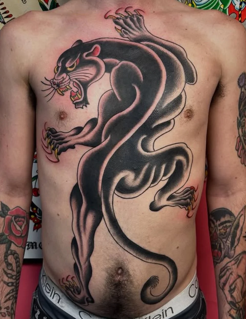 Tattoo of a black panther with yellow eyes, sharp teeth, and extended claws on a person's chest and abdomen.