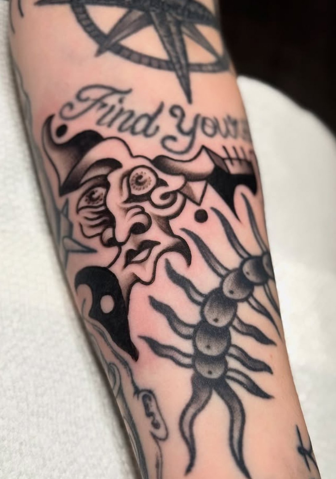 Tattoo of an abstract face, a centipede, and the phrase "Find your way" on a person's arm.