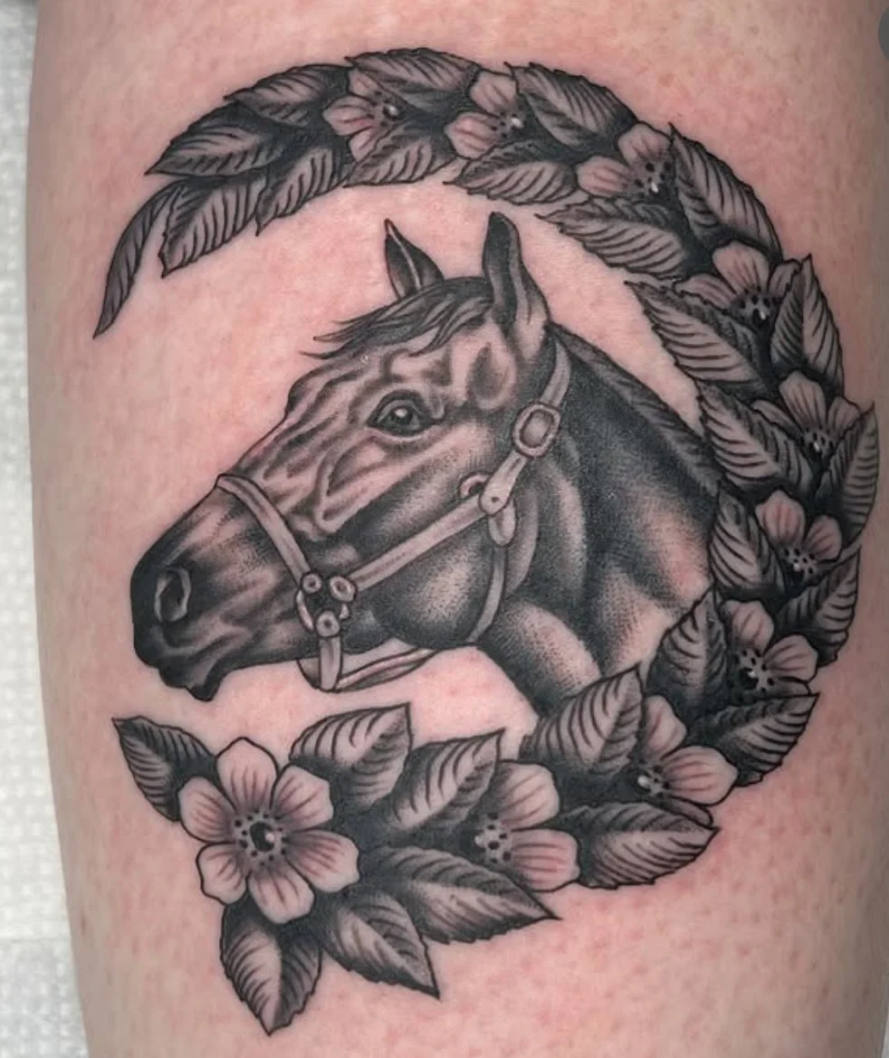 Black and gray tattoo of a horse's head surrounded by leaves and flowers.