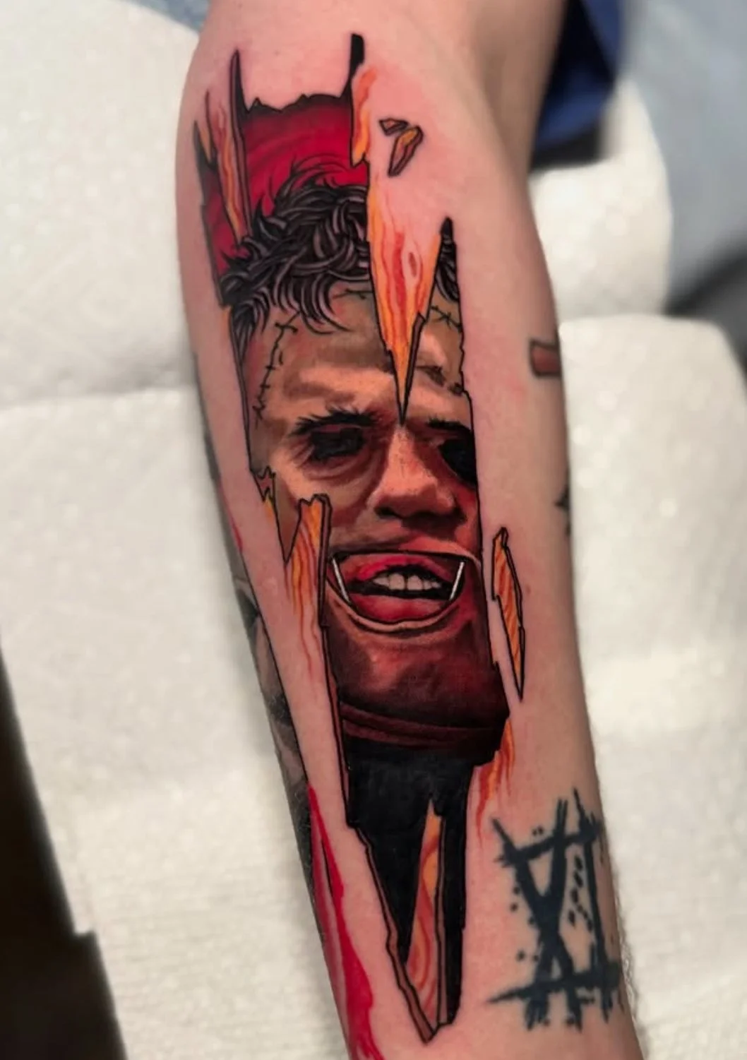 Tattoo of Leatherface with a wide smile, surrounded by stylized wood effects.
